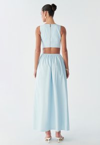 Modèle portant un top court bleu clair et une jupe maxi fluide, montrant une vue de dos contre un fond blanc uni.