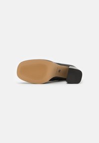 Black heel shoe with a textured, tan rubber sole. The sole is flat with horizontal grooves for grip, designed for durability.