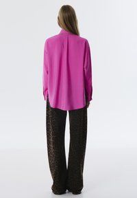 Blusa de satén rosa con un corte relajado y detalle de cadena en el escote, combinada con pantalones sueltos de estampado de leopardo marrón.