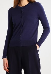 Tmavě modrý kardigan z měkké pletené látky s kulatým výstřihem, dlouhými rukávy a šesti knoflíky v odpovídající barvě po celé délce přední části.