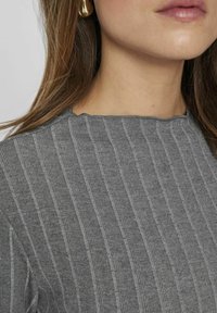 Top gris acanalado con cuello redondo y tejido texturizado. La vista de cerca ilustra las rayas verticales y un material suave y elástico.