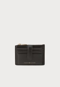 Porte-cartes en cuir noir avec une fermeture éclair dorée, plusieurs emplacements pour cartes et un rabat avant. Présente le logo "TOMMY HILFIGER" en relief sur le devant.