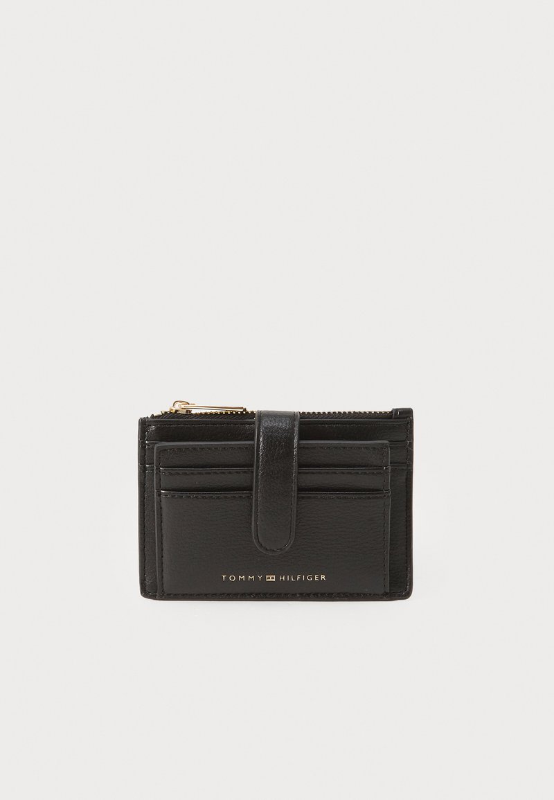 Porte-cartes en cuir noir avec une fermeture éclair dorée, plusieurs emplacements pour cartes et un rabat avant. Présente le logo "TOMMY HILFIGER" en relief sur le devant.