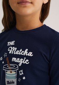 Sötétkék pamut póló fehér és színes nyomtatott szöveggel, valamint szívószálas matcha ital grafikájával és csillagokkal. Rövid ujjú.
