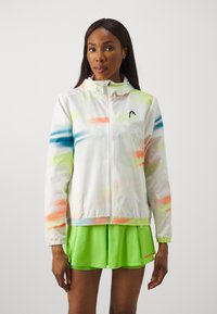 White athletic jacket with colorful splashes of blue, orange, and green. Features a hood, zippered front, and elastic hem. Paired with a green skirt.
