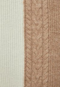Tissu de pull en tricot crème et beige clair, présentant un motif de câbles texturé sur la section marron et une texture côtelée sur la partie crème.