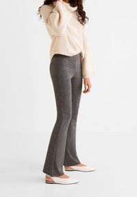 Gray flared trousers in a textured fabric, paired with a loose-fit cream knit sweater and white mules with black accents.