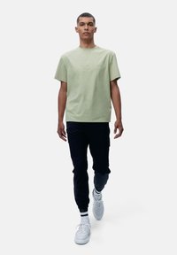 Lichtgroene katoenen T-shirt met een ronde hals, gecombineerd met donkerblauwe joggingsbroeken en witte sneakers met zwart-witte gestreepte accenten.