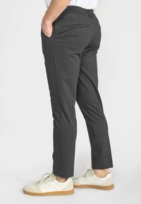 Grijze slim-fit broek met een platte voorkant, zijzakken en een strak design, gecombineerd met witte sneakers met een lichtbruin zool.