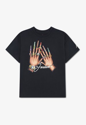 T-shirt noir avec un dessin de deux mains portant des bagues et des montres, de longs ongles décorés, et le mot "Jordan" écrit en dessous en écriture blanche.