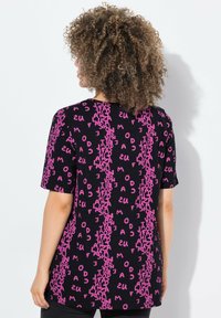 Camiseta negra de manga corta con un patrón de texto en color rosa repetido. La tela tiene una textura suave y un ajuste relajado.