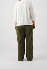 Biała bluzka z wycięciami, z rękawami do trzeciej ćwierci, zestawiona z luźnymi oliwkowymi spodniami typu cargo, które mają kieszenie boczne i prosty krój nogawek.