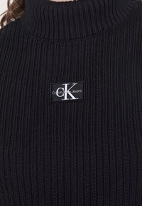 Czarny prążkowany, dziany golf z naszywką z logo Calvin Klein Jeans w kolorze białym. Materiał jest miękki, o dopasowanym kroju.