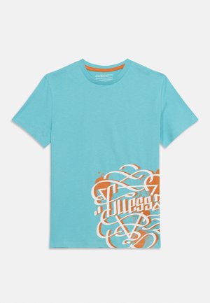 Camiseta de manga corta azul claro con diseño en espiral del logo "Guess" en naranja y blanco en el lado inferior derecho.