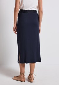 Tmavě modrá midi sukně z měkké látky, s širokým elastickým pasem s názvem značky a bočním rozparkem pro zvýraznění detailu.
