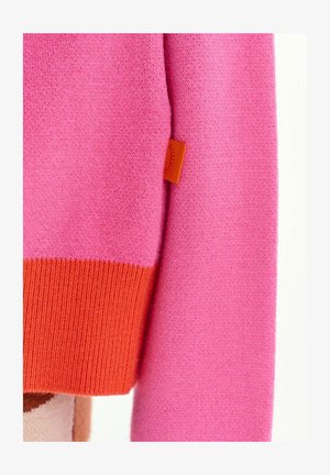 Roosa kootud kangas oranži soonikkoega varrukaotsaga ja väikese oranži sildiga, millel on päikese kujutis küljeõmblusel.