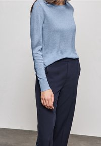 Vaaleansininen pitkähihainen neule, jossa on pyöreä pääntie ja pehmeä pinta, yhdistettynä tummansinisiin leveälahkeisiin housuihin. Mukava ja rento tyyli.