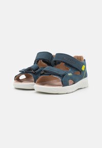 Blue leather sandals with open toe and sides, featuring two adjustable Velcro straps and a white textured sole. Subtle branding visible.