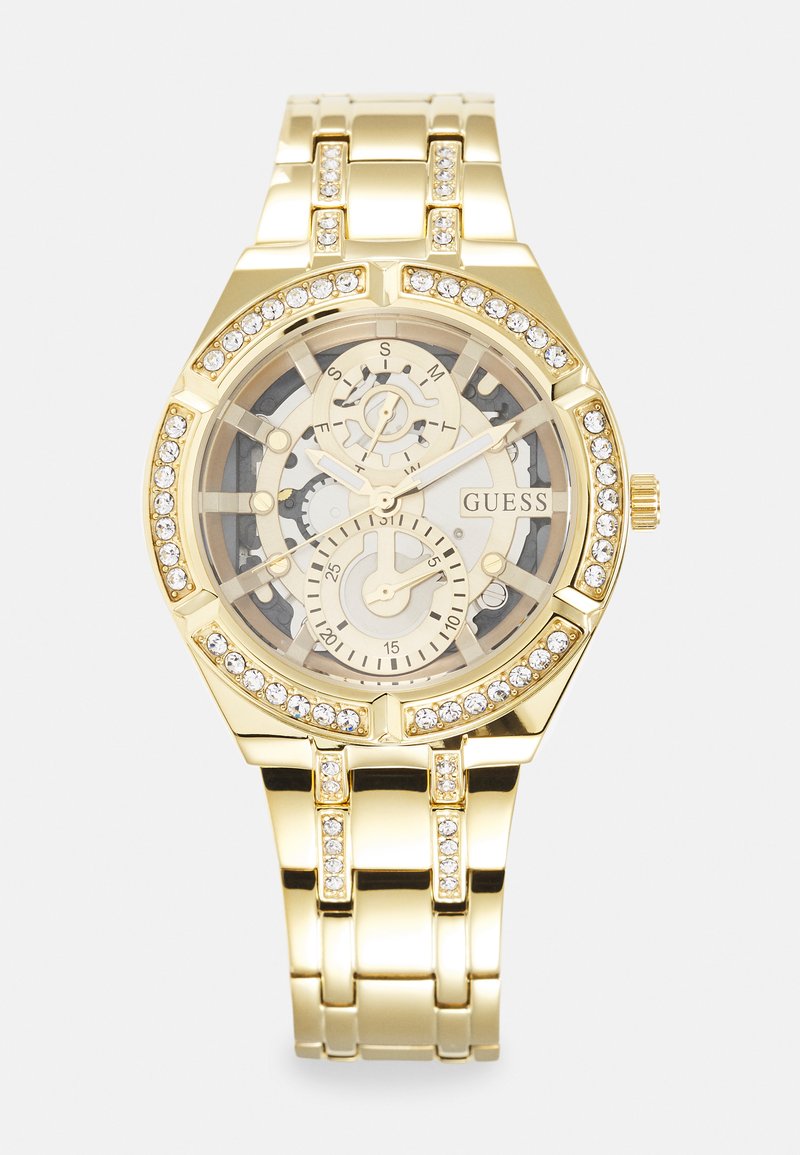 Montre en métal doré avec un cadran transparent, présentant des détails d'engrenages, trois sous-cadrans et des accents en cristal autour de la lunette et du bracelet.
