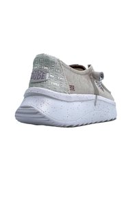 Zapatilla gris claro con acentos metálicos texturizados, suela blanca salpicada y un tirador. Presenta un diseño casual y una forma de perfil bajo.