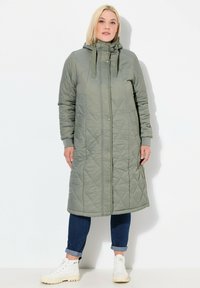 Gequilte groene lange jas met capuchon, drukknoopsluiting en zijzakken. Heeft ribgebreide manchetten en verstelbare trekkoorden. Glad, lichtgewicht materiaal.