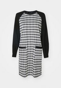 Musta-valkoinen mekko, jossa on houndstooth-kuviointi vartalolla, kiinteät mustat raglan-hihat ja kaksi etutaskua.