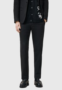 Zwarte op maat gemaakte broeken van soepel stof, met een recht model en minimale details, gecombineerd met zwarte leren schoenen.