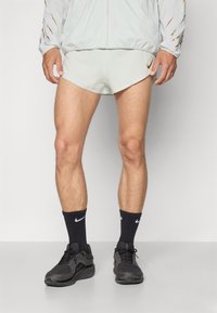 Pantalones cortos deportivos de color gris claro con un corte afilado, combinados con calcetines negros de Nike y zapatillas oscuras. Excelente chaqueta corta con acentos en los puños.