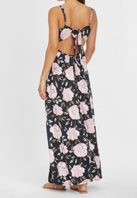 Kwiatowa maxi sukienka w granatowym kolorze z różowymi kwiatami, z regulowanymi ramiączkami i zawiązywanym tyłem. Wykonana z lekkiego materiału.
