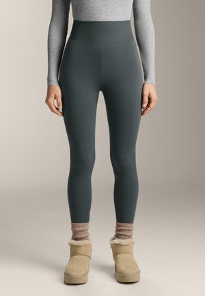 Leggings a coste grigi con vita alta di una tonalità verde scuro, abbinate a stivali alla caviglia foderati in shearling beige e calzini a coste rosa.
