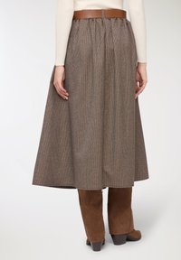 Gonna a quadri marrone con vita arricciata e cintura di pelle marrone. Il tessuto ha un motivo strutturato, abbinato a stivali marroni in suede al ginocchio.