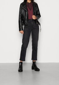 Svart läderbikerjacka över en bourgogneröd topp med spetsdetaljer, kombinerad med högmidjade svarta jeans och kraftiga svarta ankelboots.