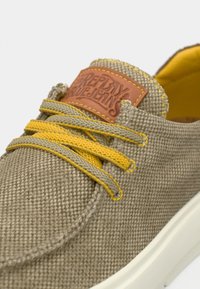 Μπεζ πάνινα παπούτσια με κίτρινα κορδόνια και καφέ δερμάτινη ετικέτα. Διαθέτουν λευκή σόλα από καουτσούκ και υφή υφασμάτινου επάνω μέρους.