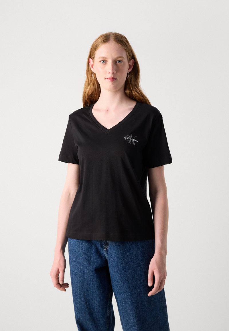 Czarna bawełniana koszulka z dekoltem w serek i krótkimi rękawami, z małym białym logo na lewej piersi. W komplecie z luźnymi niebieskimi dżinsami.