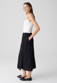 Gonna maxi nera con motivo a foglie testurizzato, cinturino elastico, tasche laterali. Abbinata a un top bianco aderente e ballerine nere.