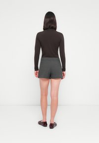 Pantaloni scurți gri dintr-un material texturat, cu un brâu lat, asociați cu un top ajustat cu mâneci lungi maro și pantofi negri lucioși.