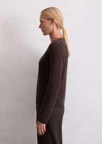 Pull en tricot marron à manches longues, surface texturée et col rond. Coupe ajustée, présenté sur un modèle devant un fond uni.