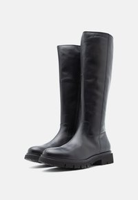 Pár vysokých čiernych kožených čižiem s hrubými gumovými podrážkami a jemným prešívaním, odfotených na bielom pozadí.