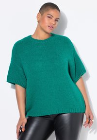 Teal strikket sweater med korte ærmer og ribbet kant. Har en afslappet pasform, blød tekstur og rund halsudskæring. Bæres sammen med sorte leggings.