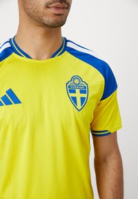 Man wearing yellow and blue Sweden soccer jersey with Sverige crest and Adidas logo, shown from neck to mid-torso.