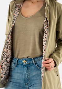 Giacca impermeabile verde oliva con interno a stampa leopardata, abbinata a una maglietta verde chiaro e jeans blu a vita alta.