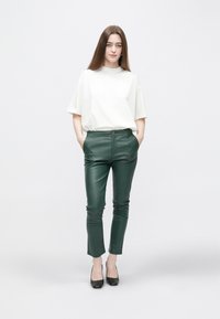 Groene broek van nep leer met een strakke pasvorm, gecombineerd met een loszittend wit T-shirt. Zwarte hakken maken de outfit compleet.