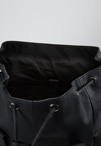 Svart texturerat läder bucket-väska med justerbar dragsko-stängning och mörkt tyginrede, som har ett litet inre fack.