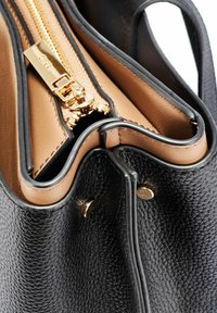 Czarna torba z teksturowanej skóry z złotym zamkiem błyskawicznym i jasnobrązowym wnętrzem. Charakteryzuje się widocznymi szwami i zaokrąglonym kształtem.