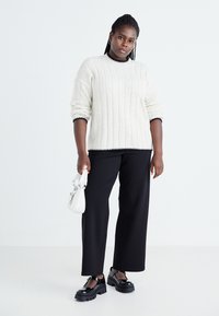 Cream ribbed sweater with black trim, black wide-leg pants, shiny black platform shoes, and a small white handbag.