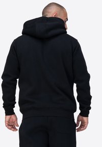 Sudadera negra con una gran capucha ajustable. Fabricada en tejido suave, cuenta con mangas largas y un dobladillo acanalado. Acabado mate sin patrones ni acentos.