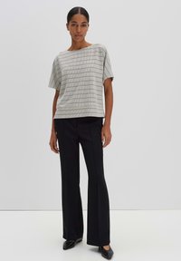 Light gray top with black geometric pattern, short sleeves; paired with high-waisted black wide-leg trousers and black slip-on shoes.