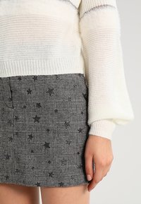 Virkat vitt tröja med ribbade muddar och svart rutigt kjol med stjärnmönster och en texturerad väv.