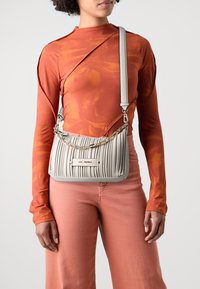 Un sac à main plissé gris clair avec des accents en chaîne, doté d'une plaque logo à l'avant ; complété par une chemise à manches longues orange et un pantalon rose.