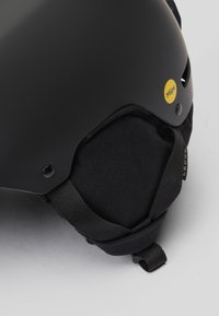 Černá lyžařská přilba s matným povrchem, štítek MIPS, nastavitelný bradový popruh a texturované polstrování. Obsahuje ventilační otvory a bezpečné upevnění.